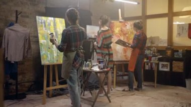 Kadın sanatçılar fırçayla tuvallere resim çiziyorlar. Boyama Atölyesi.