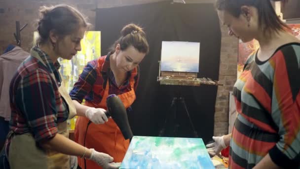 Les artistes femmes assèchent la peinture acrylique sur la toile avec un ventilateur. Collaboration artistique en atelier. — Video