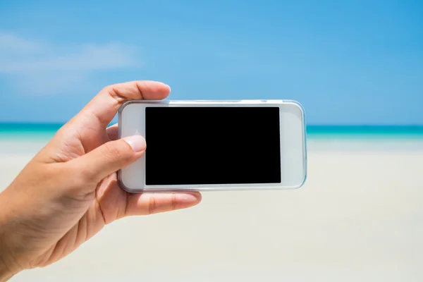 Donna mano tenere il telefono cellulare bianco con mare e cielo blu Foto Stock Royalty Free