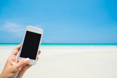 Kadın elini tut deniz ve mavi gökyüzü ile beyaz cep telefonu