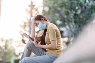 Maskeli Asyalı genç kadın elleriyle başını destekliyor..