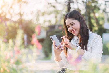Genç Asyalı kadın parkta akıllı cep telefonu, yaşam tarzı ve günlük yaşam konsepti üzerinden sosyal ağı kullanıyor.
