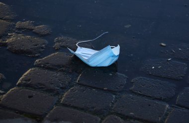 Kaldırımdaki su birikintisine atılmış kullanılmış bir tıbbi maske.