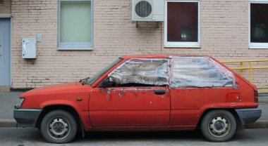 Eski bir harabe kırmızı hatchback arabası evin dışında park halinde.