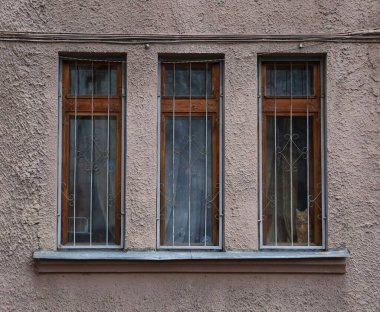 Evin duvarında üç dar parmaklıklı pencere var.