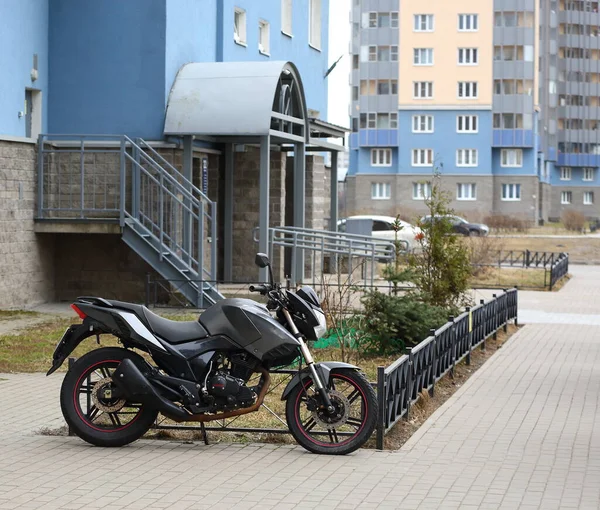 Light motorcycle parked at the lawn fence, ulitsa Belysheva, Saint Petersburg, Russia, April 2021