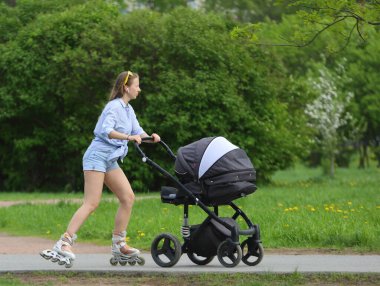 Kot şortlu genç bir anne paten sürerken yanında bir çocukla bebek arabasını iterken, Ulitsa Podvoyskogo, St. Petersburg, Rusya, Mayıs 2021