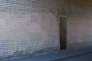 Beyaz tuğlalı bir duvarda kahverengi metal bir kapı.