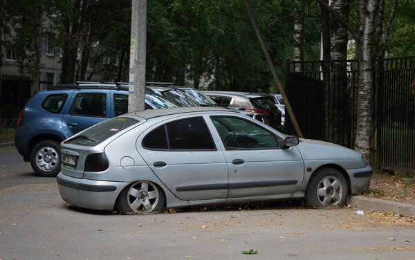 An old gray rusty abandoned car with flat wheels in the courtyard of a residential building, ulitsa Podvoyskogo, St. Petersburg, Russia, July 2021