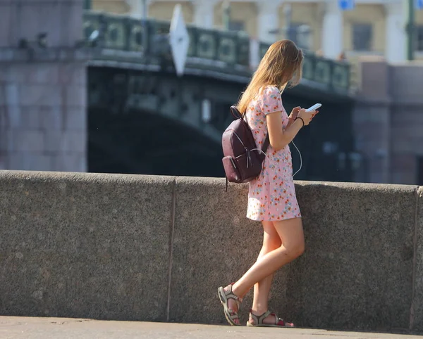2021年7月ロシアのサンクトペテルブルクにあるDvortsovaya Embankment Dvortsovaya堤防上のバックパックとスマートフォン付きの軽い夏のドレスの女の子 — ストック写真
