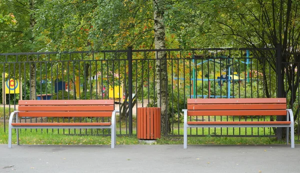 Metal bir çitin yanında beton vazo olan iki kahverengi ahşap park bankı.