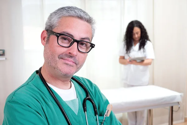 Medico guardando macchina fotografica e infermiera di lavoro — Foto Stock