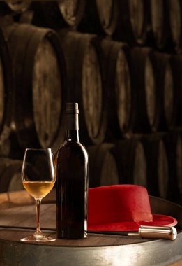 Bottle and glass of fino white sherry wine in winery with typical Jerez and Venetian red hat on the table against the background of old barrels vertical clipart
