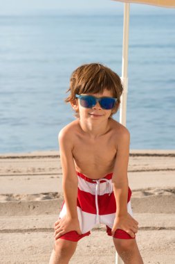 Çocuk güneş gözlüğü ile şemsiyesi altında sahilde