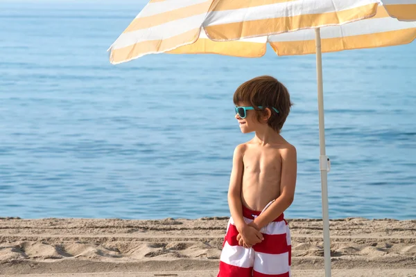 Çocuk isteyen güneş gözlüklü şemsiyesi altında sahilde