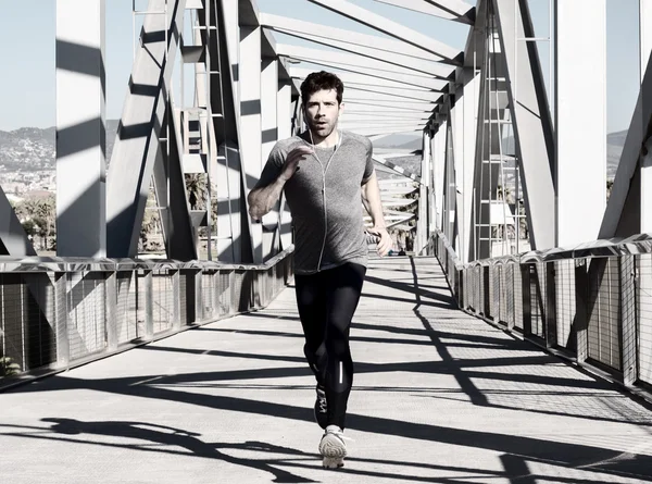 Young man running with earpieces by metal bridge — Stock Photo, Image