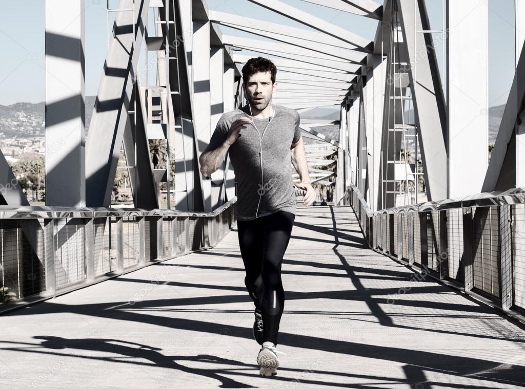 young man running with earpieces by metal bridge