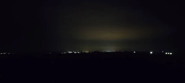 遠くにいくつかのライトで街の後ろの暗い夜星のない空暗い夜パノラマ — ストック写真