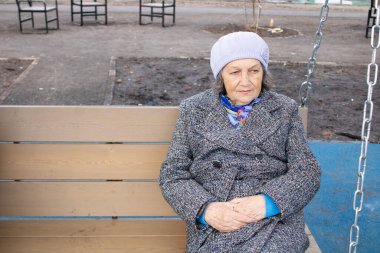 Yaşlı bir kadın salıncakta oturuyor. Paltolu yaşlı bir kadın. Büyükanne temiz havada..