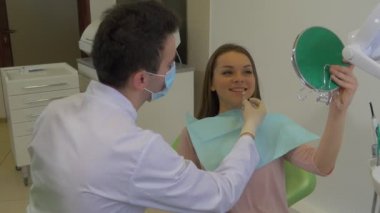 Maskeli Diş Hekimi Hasta Genç Kadın İçin Yeni Diş Rengi Seçmeye Çalışıyor Ona Ayna Tutuyor Ve Diş Tedavi Odasında Gülümsüyor
