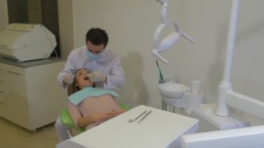 Young Dentist Takes a Tools Examining a Teeth Dentist in Mask is Sitting Behind a Client Woman and Working Concentratedly at Dental Treatment Room