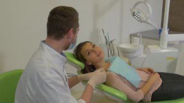 Hasta Kızla Konuşan Diş Hekimi Ayağa Kalkar Gülümseyerek Bir Elini Sallıyor Maskeli Bir Klinik Diş Hekiminden UzakLaşıyor Diş Tedavi Odasında Hasta Ayakta