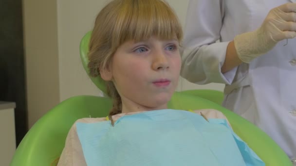 Chica paciente en una silla dentista pone una succión en su boca dentista en máscara está examinando un diente de un paciente en la sala de tratamiento dental Visita al dentista — Vídeo de stock