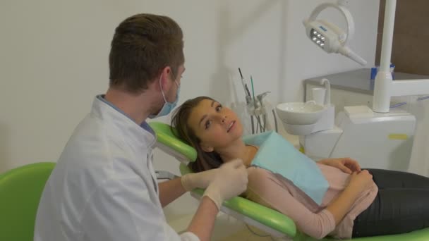 Dentista hablando con paciente chica se levanta sonriendo se sacude una mano se aleja de una clínica Dentista en máscara es paciente de pie en la sala de tratamiento dental — Vídeo de stock