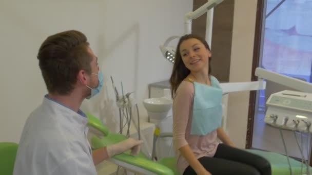Пацієнт стоїть вгору посміхаючись тремтить рукою від клінічного стоматолога в масці стоїть пацієнт в стоматологічній клініці Візит до стоматолога — стокове відео