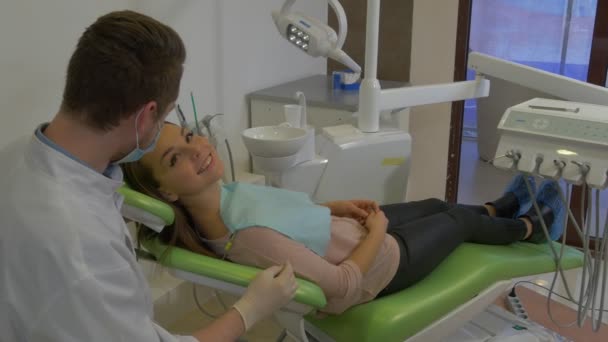 Zubař mluví s klientem a dává jí zrcadlovou ženu usmívající se pohled na zrcadlový doktor sedí za pacientovu hlavní klinikou — Stock video