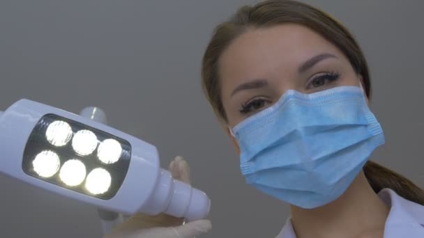 マスクアプローチの歯科医は、患者の医師が歯の歯科医院を検査する手袋でラボコートの手に身を包んだ上に立ってフックを保持しています — ストック動画