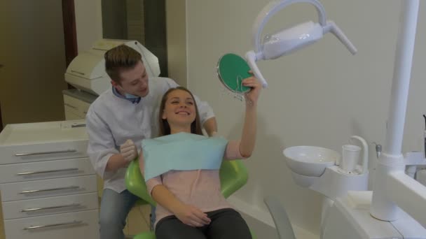 Woman is Looking at Mirror Dentist is Talking Young Male Doctor and Female Client of a Dental Clinic in a Chair Happy Client Visit to a Stomatologist — Vídeo de Stock