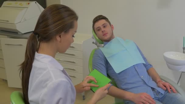 Paciente toca um dentista mandíbula menina pergaminhos Tablet Ouvindo um homem cliente está falando reclamações quarto de clínica dentária jovem médico feminino cliente masculino — Vídeo de Stock