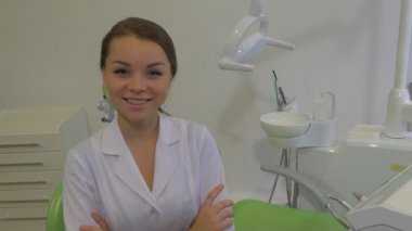 Dostu Diş Hekimi Genç Kadın Oturan Crossed Arms Lab Coat Girl Kamera Diş Hekimi Makine Diş Lambası Yeşil Sandalye Diş Kliniği bakarak Gülümsüyor