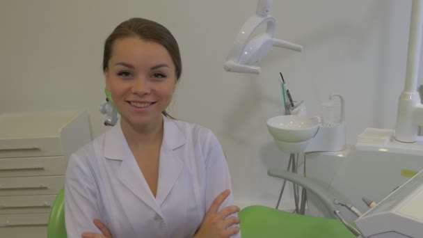 Przyjazny dentysta młoda kobieta siedzi skrzyżowane ramiona laboratorium płaszcz dziewczyna jest uśmiechnięta patrząc na aparat dentysta maszyna Lampa stomatologiczna Zielona krzesło Dental Clinic — Wideo stockowe