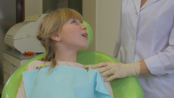 Dentista está tratando um paciente de dentes de criança sentado em uma cadeira verde Doutor está segurando uma sucção e gancho Kid não gosta de uma visita de tratamento a um dentista — Vídeo de Stock