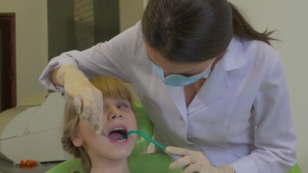 Fogorvos kezeli a Kid 's fogak Kid is nyalás Lips ül egy zöld szék doktor Holding a szívó-és Hook fogászati klinika látogatás a fogorvos — Stock videók