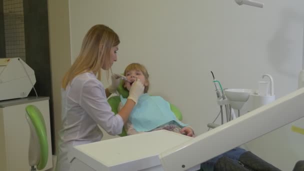 Mujer dentista está examinando un diente con espejo Paciente Adolescente Niña está sentada en una silla verde Mujer doctora pone un instrumento cambia la clínica de la mesa — Vídeo de stock