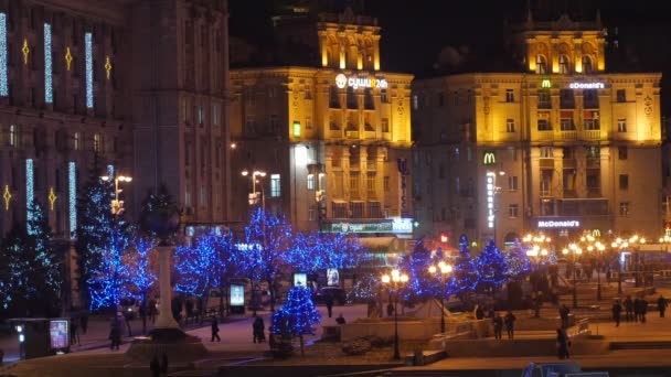 Pessoas caminhando ao longo de edifícios vintage na Praça da Independência na véspera de Ano Novo Iluminado Park Alley Blue Christmas Lights on a Trees Night Holiday — Vídeo de Stock