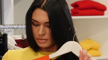 Kadın bir turuncu elbise seyir çalışıyor ayna seçen giyim kadın giyim Dükkanı mutlu istemci esmer kadın bir butik giysilerle satın alıyor