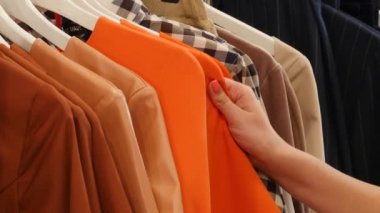 Woman is Looking at Orange Dresses on a Trempels Choosing a Clothes Womenswear Shop Client Brunette Woman is Buying a Clothes in a Boutique Garments