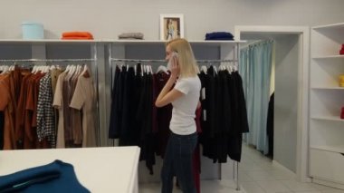 Woman Enters to Shop Talking by Phone Chose Dress Smiling Tries it Womenswear Shop Client Blonde Woman is Buying a Clothes Garments on a Trempels