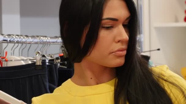 Donna che tiene il vestito arancione tocca il materiale La scelta di un abbigliamento Donna su Trempelss Shop Cliente Bruna Donna sta comprando un abbigliamento in una boutique — Video Stock