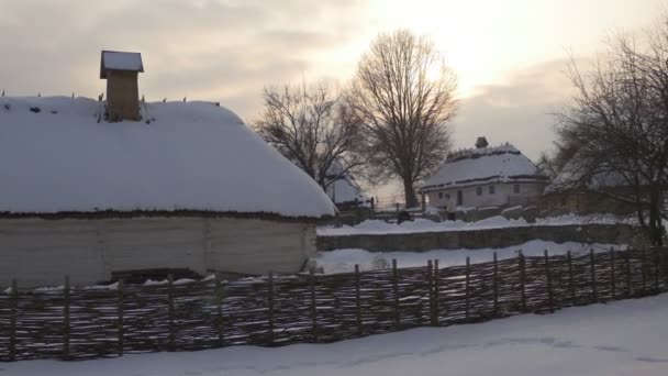 Malé rustikální domy s přílním plotem kolem nich na Wintry krajina v Pirogovské vesnici sníh na střechách scenérie venkovského západu slunce Ukrajina — Stock video