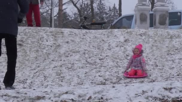 Familia montando trineo Navidad Bucha Ucrania Chica está montando en un trineo rosa cuesta abajo Invierno Los niños y los padres pasan tiempo juntos Diviértete en el parque — Vídeos de Stock