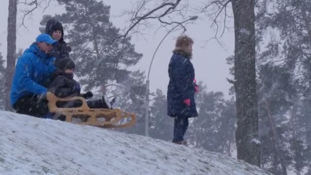 Kerstmis in Bucha Oekraïne ouders duwen een slee kinderen rijden op een slee Downhill winter ouders zijn het nemen van foto families tijd samen doorbrengen — Stockvideo