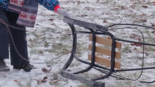 Kind trekt een slee bergopwaarts langzaam door sneeuw in City Park Bucha Oekraïne Kerst Winter ouders zijn op een heuvel gezinnen tijd samen doorbrengen — Stockvideo