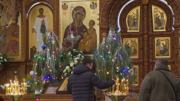 Man korsar cameraman Dormition Cathedral Christmas WORSHIPER framför ikonen brinnande ljus Holy Mountain Lavra Ukraina dekorerade granar Golden Decor — Stockvideo