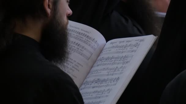 Clergé à l'église Noël Sainte Montagne Lavra Dormition Cathédrale Foule d'hommes barbus en vêtements noirs chantent debout tenant un recueil de chansons — Video