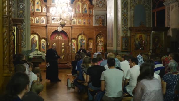 Volk en geestelijken in Heilige Drievuldigheid Jona's Klooster Kiev Oekraïne Dormition van een Mary interieur van een orthodoxe kerk mensen zitten op een banken luisteren — Stockvideo